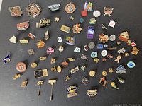 Full view of mixed pins arranged on a dark surface showing a variety of designs including sports, promotional, and decorative pins