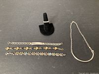 Photo showing the silver ring on a ring display and the silver choker necklace on the right with three bracelets below them. The bracelets include a solid curb chain, a heart and blue heart-shaped stone linked bracelet, and a multi-colored stone geometric linked bracelet.
