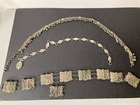 Photo showing all three vintage metal belts laid out flat on a dark surface to display overall length and style.