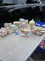 Full view of 9 baby themed ceramic planters on a table including animals, dolls, and baby items mainly in pastel colors.