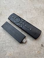 Photo of Amazon Fire TV Stick streaming device and remote control on a textured surface.