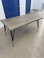 Full view of the rectangular dining table showing the smooth solid tabletop surface with slightly rounded edges and black iron legs with gold-tone tips.
