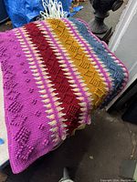 Folded and draped view of the blanket showing colorful textured knit pattern with stripes of pink, red, yellow, and blue