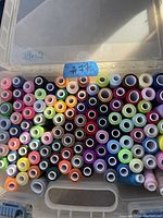 Top-down view of a plastic container filled with multiple colorful sewing thread spools, arranged in rows.