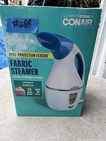 Original boxed Conair fabric steamer showing front panel of the box including key features: spill protection, 1100 watts, 60 second heat up, suitable for travel.