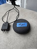 Google Home Mini smart speaker alongside Motorola charger and power cable lying on a plastic surface, showing condition and included components.