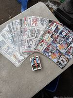 Spread of hockey cards arranged in plastic sleeve pages alongside a smaller pile of loose cards on a table, showcasing various hockey players.