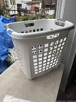 White laundry hamper placed on a concrete surface near a wall and outdoor area.