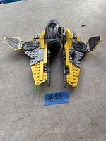 Top view of assembled LEGO Star Wars Anakin's Interceptor model with yellow and black wings and clear cockpit canopy on grey surface.