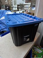 Mastercraft heavy-duty storage tote with black body and blue lid shown outdoors on a table