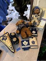 Wide view showing all items including plush bear, doll, pennant, dice, and koozies laid out on table