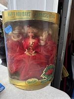 Photo of the 1993 Happy Holidays Barbie doll in original packaging. The doll is dressed in a red festive gown with glitter, with the box showing age wear but sealed.