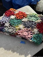 Photo of a folded vintage hand crocheted blanket laid on a gray surface, showing multicolored yarn with snowflake or star-shaped crochet motifs.