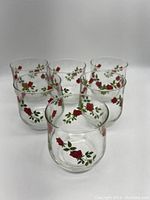 Photo showing six drinking glasses in circular arrangement decorated with red climbing roses and green leaves.