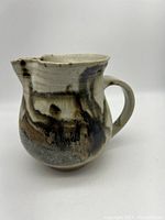 Full side view of ceramic pitcher showing handle and spout, glazed in a pattern with browns, blacks, and creams.