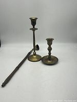 Photo showing two brass candle sticks of different heights next to a long candle snuffer with wooden handle.