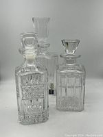 Front view of three clear glass decanters with distinct cut designs and stoppers arranged in a triangular layout against a white background.