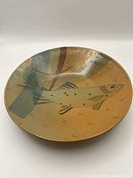 Top view of the round ceramic plate/bowl showing fish design with earth tones and blue shading.
