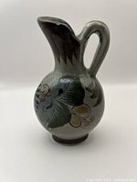 Front and side views of the grey Tonala ceramic pitcher showing hand-painted leaf and berry decoration and the shape of the spout and handle.