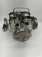 Front view of the six highball tumblers inside the silver caddy with coasters attached on sides