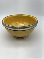 Side view showing the yellow glazed ceramic bowl with silver metal rim and small foot ring.