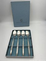 Four Oneida Community spoons with textured handles in blue box with compartments.