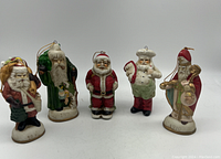 Photo of five vintage style Santa Claus figurines with different designs and years marked on bases, displayed in a row.