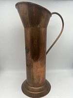 Front side view of the tall copper pitcher showing the curved brass handle and cylindrical body.