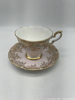 Side view of the porcelain tea cup highlighting its pink exterior, gold gilt handle, and gold decorative pattern near the rim.