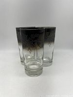 Front view of three clear highball glasses with silver fade rims and etched rose floral patterns.