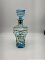 Front view of vintage blue Argento glass decanter with gold floral accents and stopper.