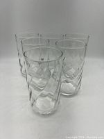 Six clear Libbey glasses with raised swirl pattern, set standing on a white surface, photo angled.