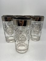Front view of three highball glasses showing platinum rim and etched decorative scrollwork on clear glass.