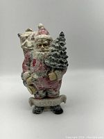 Front view of glittered vintage Santa Claus figurine holding Christmas tree and sack with visible face details and base.
