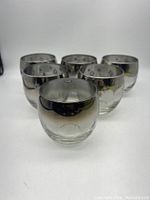Front view of six roly poly glasses with silver luster rims and starburst design, arranged with one glass in front and five behind.