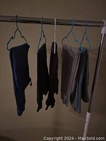 Five pairs of boys pants hanging on hangers including sweatpants and jeans in assorted colors.