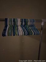 Side view of a collection of kids plastic hangers grouped on a metal clothing rod, showing mix of blue, white, and green hangers.