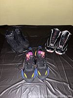 All three pairs of sneakers displayed on a black cloth background: one pair black with blue accents, one pair black with white and red detail, one pair Puma black with colorful accents.