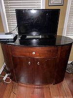 Front view of the wooden credenza cabinet with black glass top and silver hardware, showing scratches and wear on the wood surface.
