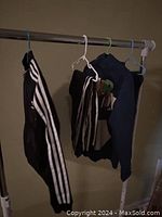 Photo showing two boys clothing items hanging on a rack: black Adidas pants with white stripes and navy blue Jordan hoodie with colorful text on the back.