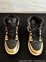 Front view of black and gold Air Jordan sneakers with Jumpman Air logo on tongue and black laces visible.