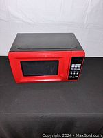Front top and side view of a red microwave oven with black control panel keypad.
