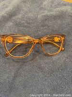 Front view of Versace eyeglasses lying on a blue textured cloth, showing the rose clear cat-eye frames and gold logo details on the arms.