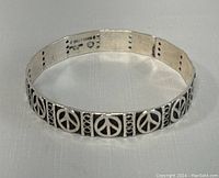 Full view of silver bangle cuff bracelet featuring repeated peace sign motifs along band.