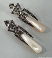 Pair of Art Deco style silver earrings with marcasite and pearlescent drops on neutral cloth background, showing front view.