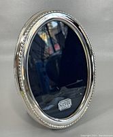 Oval English sterling silver photo frame standing upright showing reflective silver and beaded edge detail.