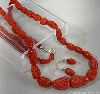 Close-up of natural coral beads show pitted texture and 925 silver clasp on necklace with matching earrings set beside it.