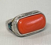 Front side view of the silver ring with prominent rectangular coral stone and textured border.