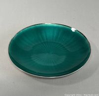 Top angled view of small round sterling silver dish with green guilloche enamel interior, showing glossy finish and subtle sunburst pattern.