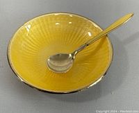 Small yellow guilloche enamel dish with matching spoon inside it, showing overall appearance and condition.